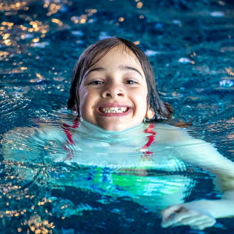 young girl with head poking out of swimming pool smiling