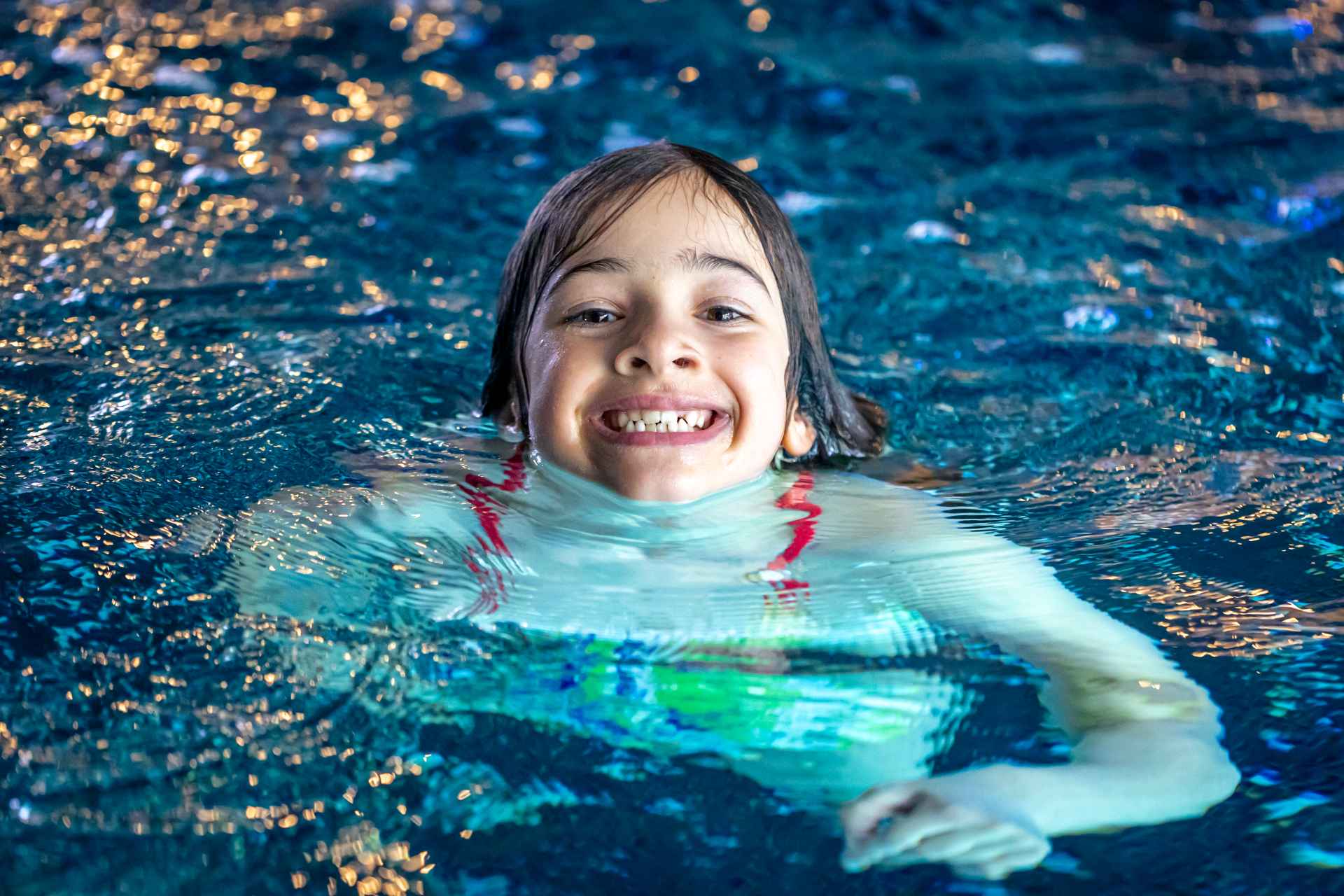 young girl with head poking out of swimming pool smiling