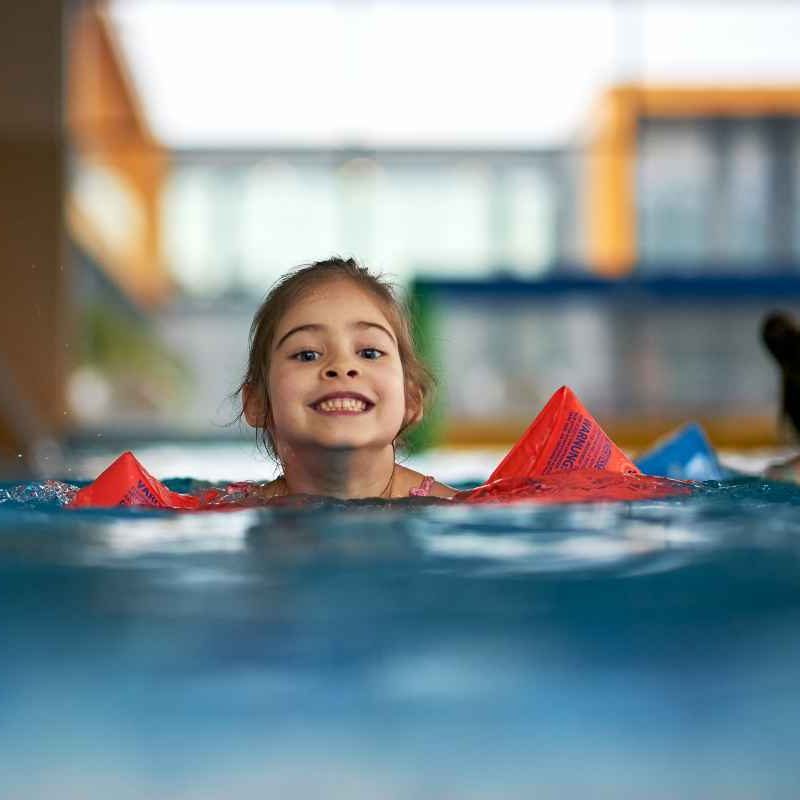 young girl smiling swimming towards shot wearing arm float devices