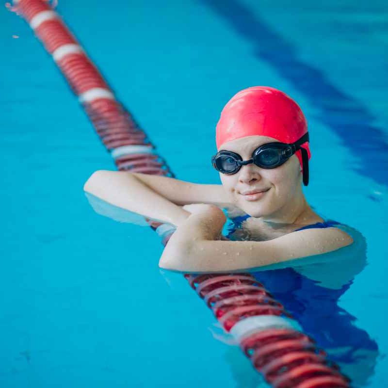 young girl in googles and swim cap in pool leaning on float line